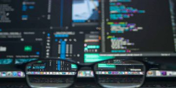 Occhiali in primo piano con dietro Pc infetto da nuovo malware