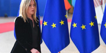 Giorgia Meloni davanti a delle bandiere dell'Unione europea