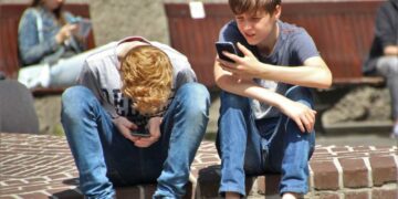 Due adolescenti seduti su un muretto che chiacchierano guardando il cellulare