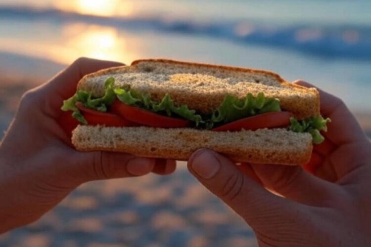 Una persona intenta a mangiare un panino in spiaggia