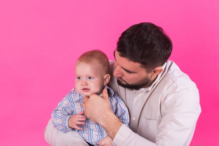 Baby in the daddy hands. Pink background