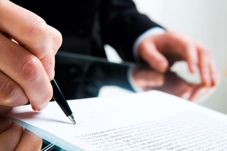 Closeup of business lady’s hand with pen signing a contract on the background of her other hand touching the table