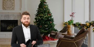 Un uomo con in mano un portafoglio vuoto davanti a un albero di Natale