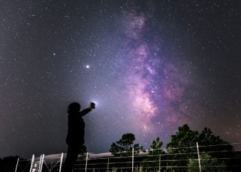 Una persona intenta a guardare le stelle con uno smartphone in mano
