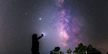 Una persona intenta a guardare le stelle con uno smartphone in mano