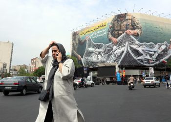 A woman walks next to an anti-US billboard reading in Persian 'The Strait of Hormuz will remain closed' at the Enghelab square in Tehran, Iran, 12 April 2026
