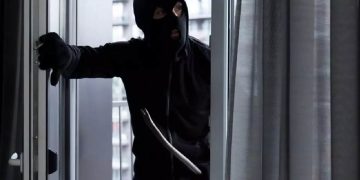 Immagine di un ladro con passamontagna che entra da una finestra con un piede di porco, utilizzata per illustrare il fenomeno dei furti in casa senza segni di scasso