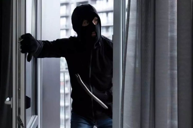 Immagine di un ladro con passamontagna che entra da una finestra con un piede di porco, utilizzata per illustrare il fenomeno dei furti in casa senza segni di scasso