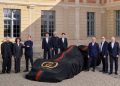 Auto con telo nero firmato Gucci Racing e dettagli verde-rosso durante la presentazione della partnership tra Gucci e Alpine in Formula 1, circondata dai dirigenti dei due brand in un cortile storico.