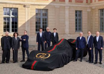 Auto con telo nero firmato Gucci Racing e dettagli verde-rosso durante la presentazione della partnership tra Gucci e Alpine in Formula 1, circondata dai dirigenti dei due brand in un cortile storico.