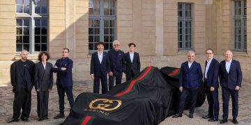 Auto con telo nero firmato Gucci Racing e dettagli verde-rosso durante la presentazione della partnership tra Gucci e Alpine in Formula 1, circondata dai dirigenti dei due brand in un cortile storico.