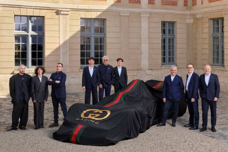 Auto con telo nero firmato Gucci Racing e dettagli verde-rosso durante la presentazione della partnership tra Gucci e Alpine in Formula 1, circondata dai dirigenti dei due brand in un cortile storico.