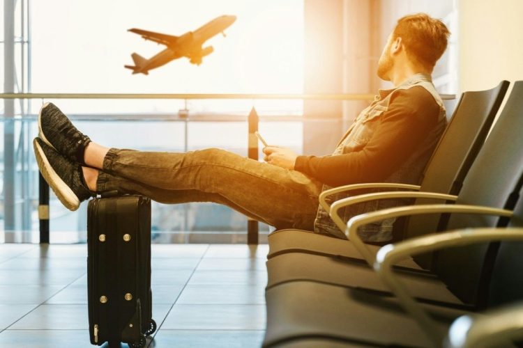 Uomo seduto in aeroporto mentre aspetta al gate. Ue, nuove regole su bagagli a mano: più trasparenza e tariffe standard per i voli