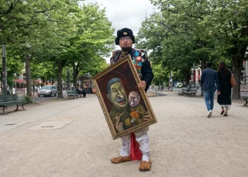 Semyon Skrepetsky vestito in costume russo espone quadro con caricature di Stalin e Putin