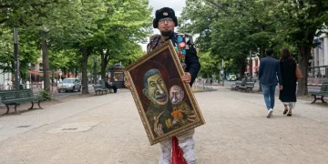 Semyon Skrepetsky vestito in costume russo espone quadro con caricature di Stalin e Putin