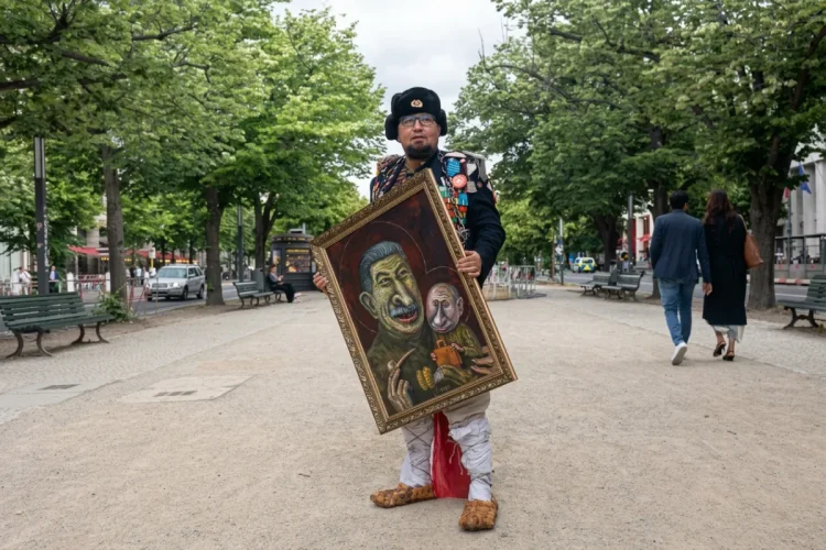 Semyon Skrepetsky vestito in costume russo espone quadro con caricature di Stalin e Putin