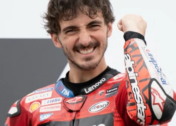 Francesco Bagnaia sorride in tuta da corsa rossa mentre alza il pugno.
