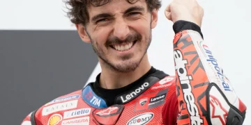 Francesco Bagnaia sorride in tuta da corsa rossa mentre alza il pugno.