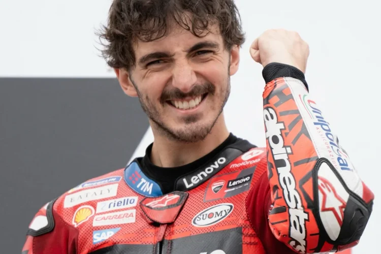 Francesco Bagnaia sorride in tuta da corsa rossa mentre alza il pugno.
