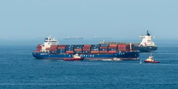 Grande nave portacontainer scortata da rimorchiatori nello stretto di Hormuz.
