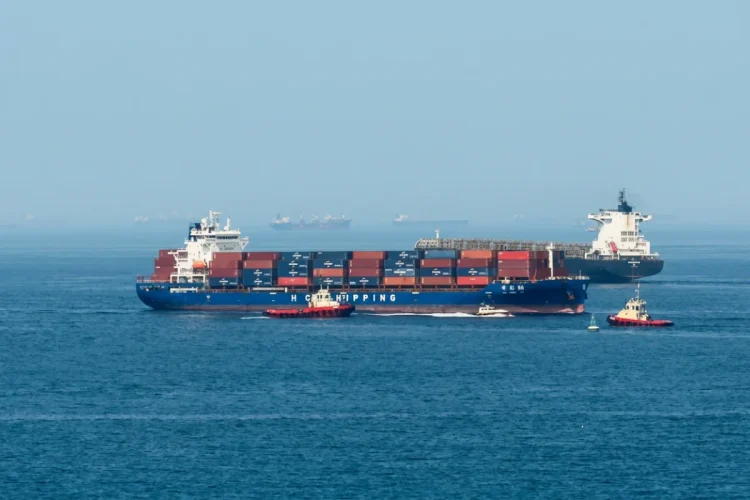 Grande nave portacontainer scortata da rimorchiatori nello stretto di Hormuz.