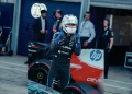 Kimi Antonelli con casco e tuta accanto alla sua auto F1 nel box