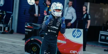Kimi Antonelli con casco e tuta accanto alla sua auto F1 nel box
