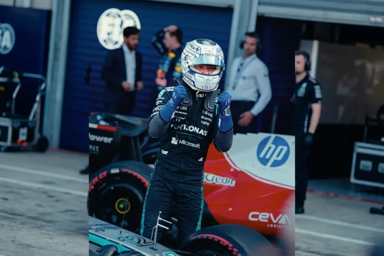 Kimi Antonelli con casco e tuta accanto alla sua auto F1 nel box