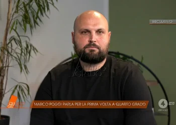 Marco Poggi calvo e barbuto in intervista televisiva, sfondo chiaro