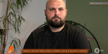 Marco Poggi calvo e barbuto in intervista televisiva, sfondo chiaro