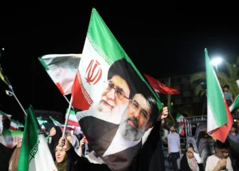 Manifestanti iraniani sventolano bandiere con i volti di Khamenei e Raisi.