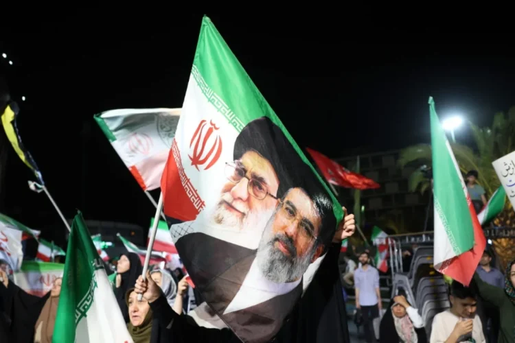 Manifestanti iraniani sventolano bandiere con i volti di Khamenei e Raisi.