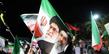 Manifestanti iraniani sventolano bandiere con i volti di Khamenei e Raisi.