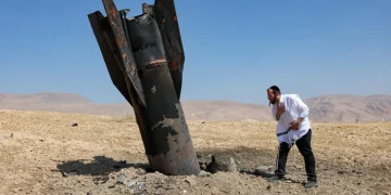 Uomo ebreo osserva inquieto detriti di missile balistico nel deserto.