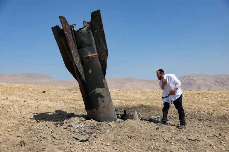 Uomo ebreo osserva inquieto detriti di missile balistico nel deserto.