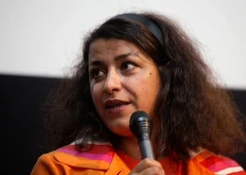 Una donna mediorientale con fascia per capelli tiene un microfono.
