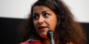 Una donna mediorientale con fascia per capelli tiene un microfono.