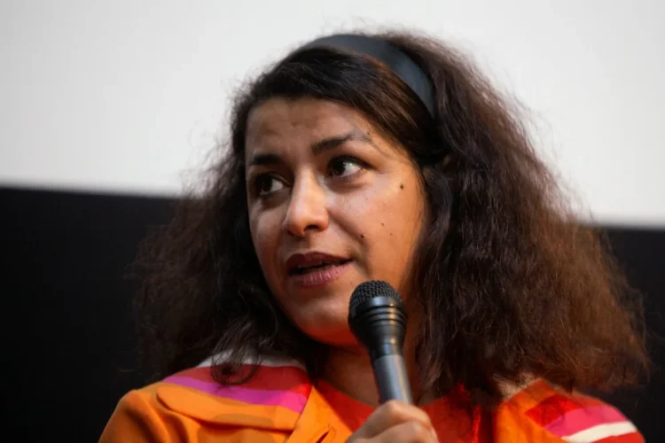 Una donna mediorientale con fascia per capelli tiene un microfono.