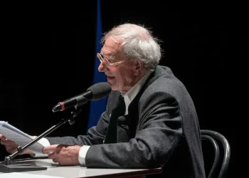 Romano Montroni legge documenti al microfono durante convegno