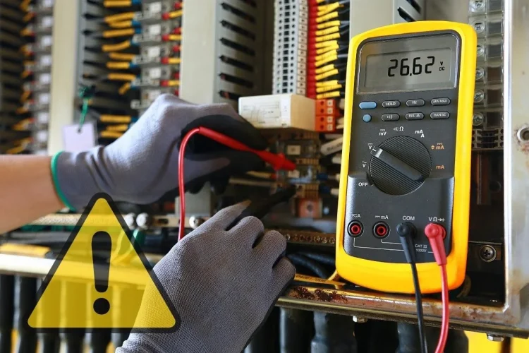 Elettricista misura tensione elettrica con multimetro giallo in un impianto.