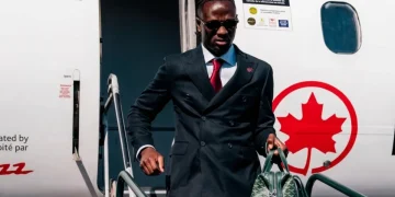 Ismaël Koné scende da un aereo in abito elegante con borsa