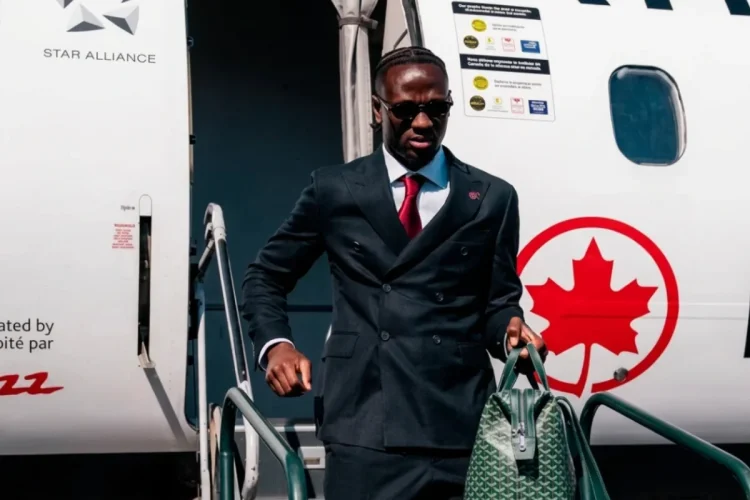 Ismaël Koné scende da un aereo in abito elegante con borsa