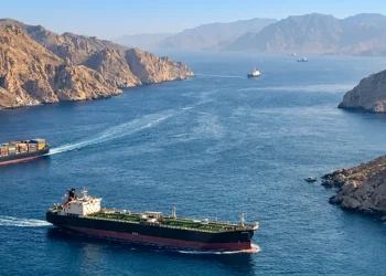 Nave petroliera e portacontainer attraversano lo Stretto di Hormuz tra montagne rocciose.