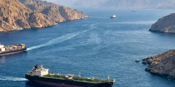 Nave petroliera e portacontainer attraversano lo Stretto di Hormuz tra montagne rocciose.