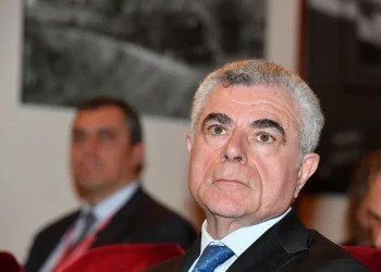 Mauro Moretti in primo piano con giacca e cravatta blu.