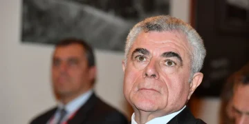 Mauro Moretti in primo piano con giacca e cravatta blu.