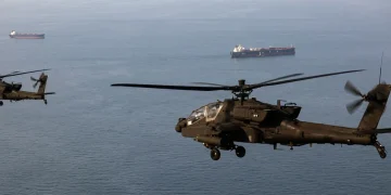 Elicotteri Apache militari sorvolano, a bassa quota, navi mercantili nello Stretto di Hormuz.