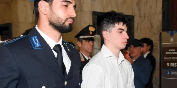 Ragazzo con camicia bianca scortato da un carabiniere in tribunale.