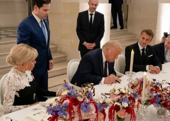 Donald Trump firma documento circondato da Emmanuel Macron e Brigitte Macron