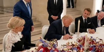 Donald Trump firma documento circondato da Emmanuel Macron e Brigitte Macron